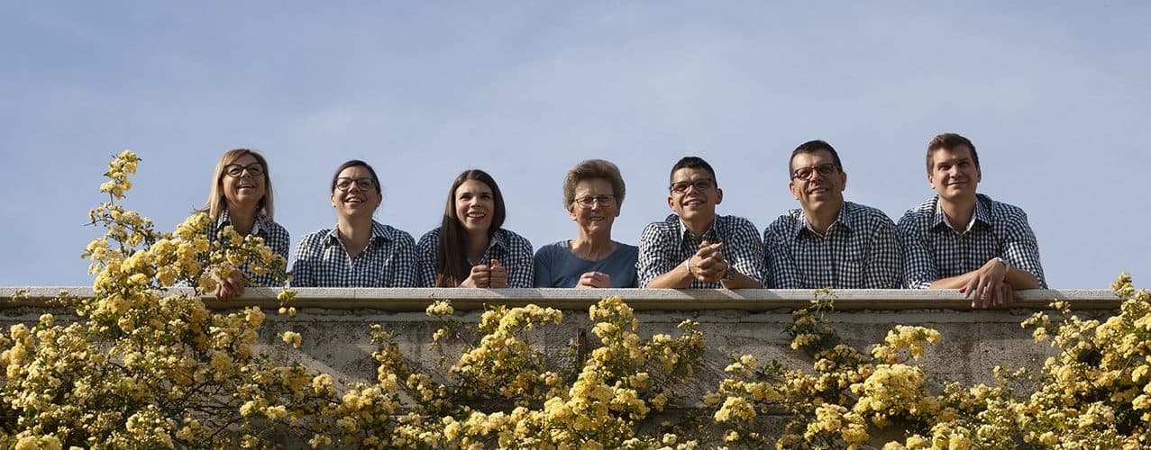 Družina Pucer za kamnitim zidom z rožami pred hišo Padnjec